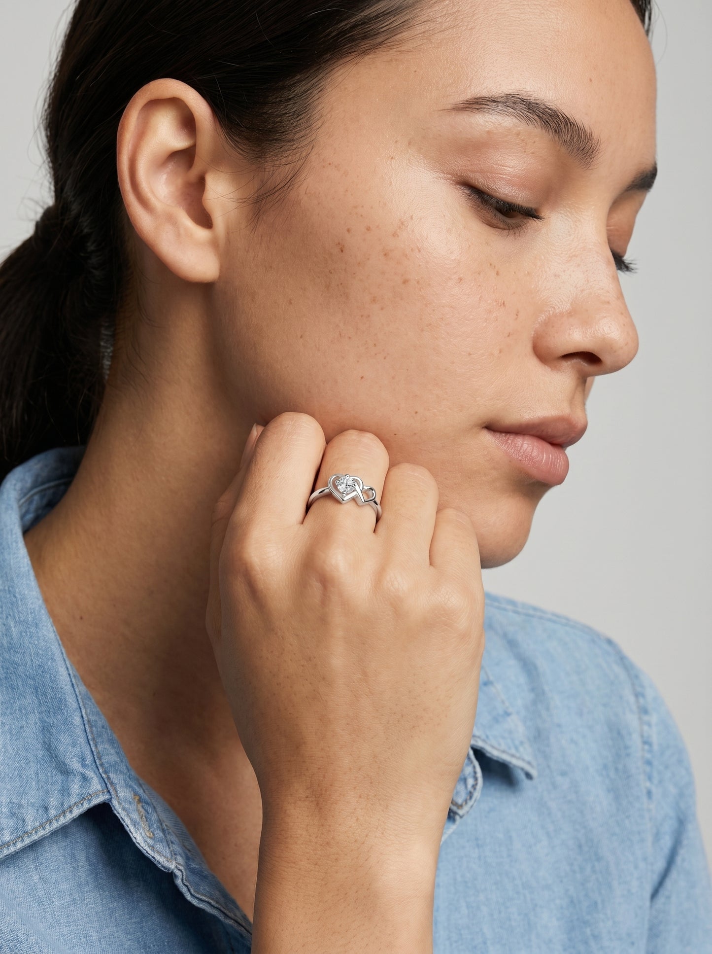 Mulher a usar um anel com uma pedra preciosa azul em forma de coração sobre um fundo neutro.