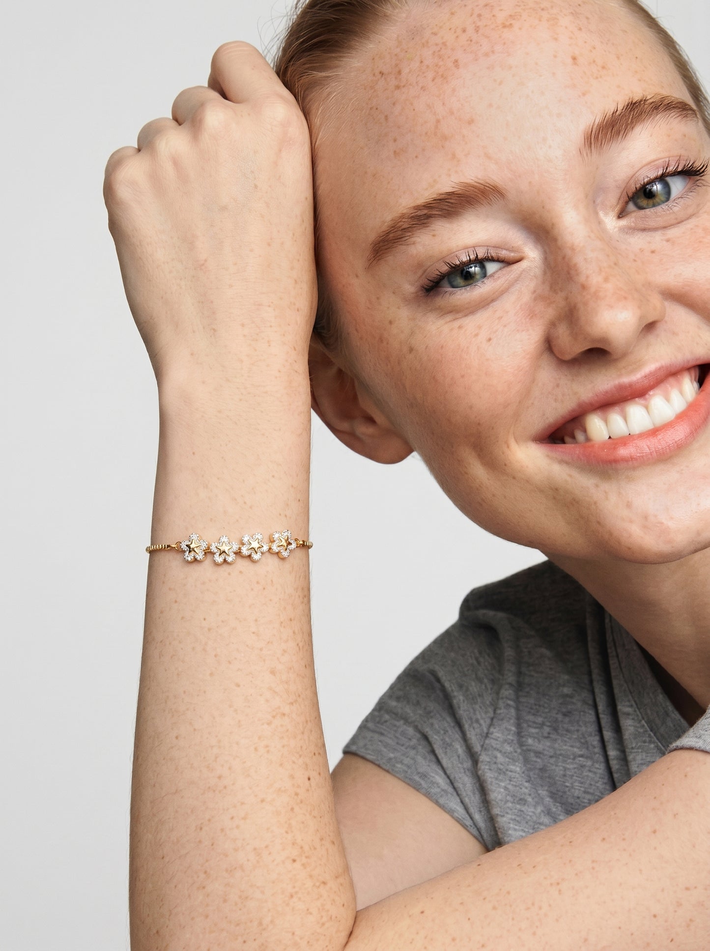 Pulseira dourada delicada com flores em cristais e corrente fina, usada por uma modelo para um visual feminino, elegante e luminoso.