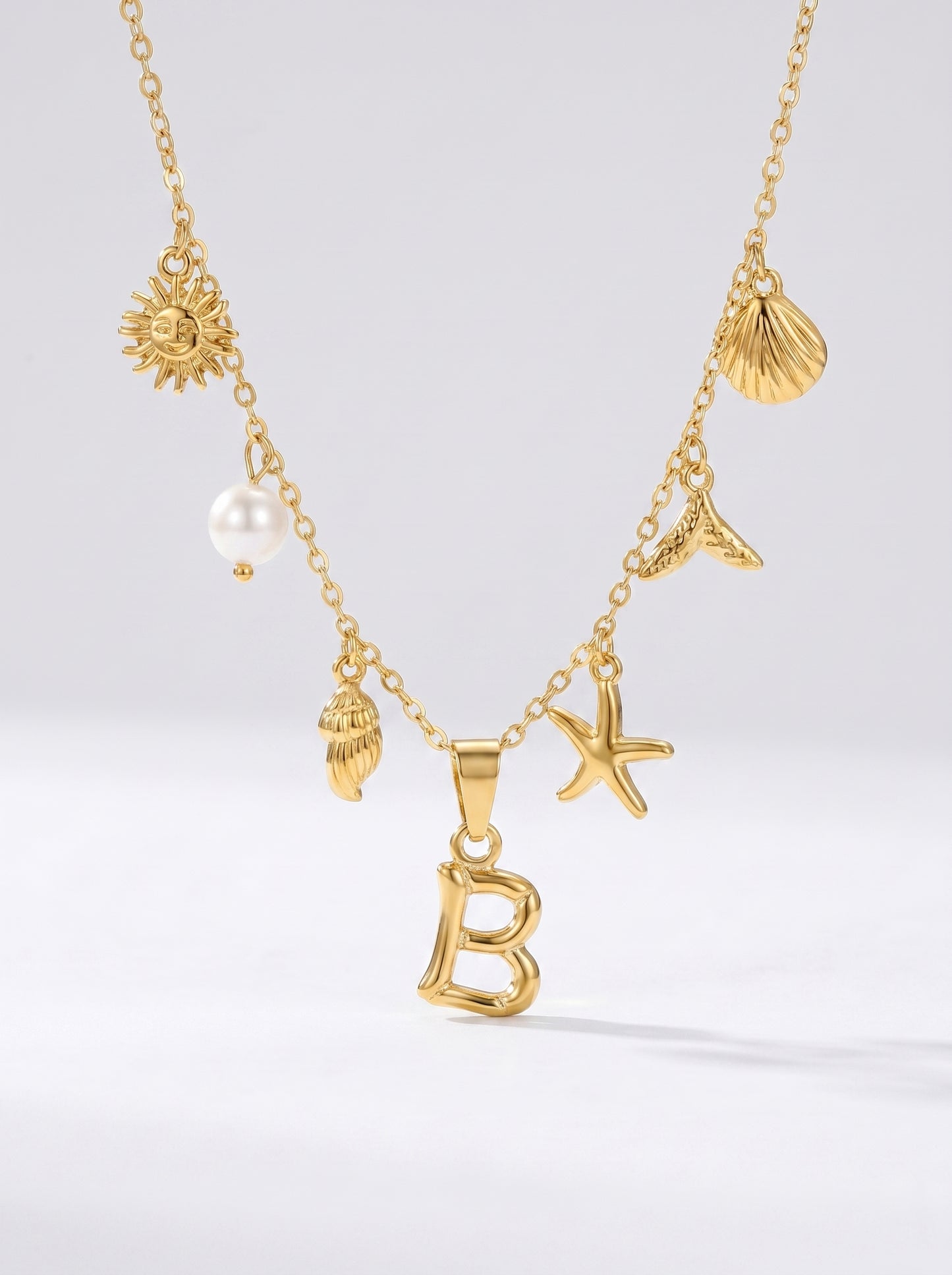 Colar dourado do mar com letra inicial B, estrela-do-mar, conchas, pérola e pendente de sol.