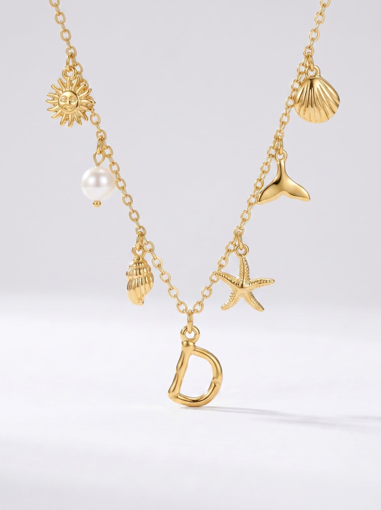 Colar dourado do mar com letra inicial D, estrela-do-mar, conchas, pérola e pendente de sol.