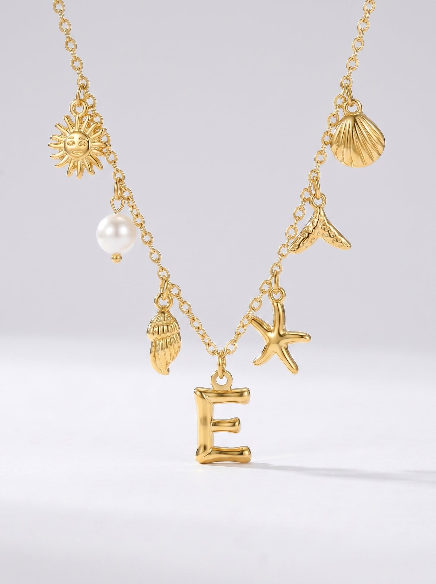 Colar dourado do mar com letra inicial E, estrela-do-mar, conchas, pérola e pendente de sol.