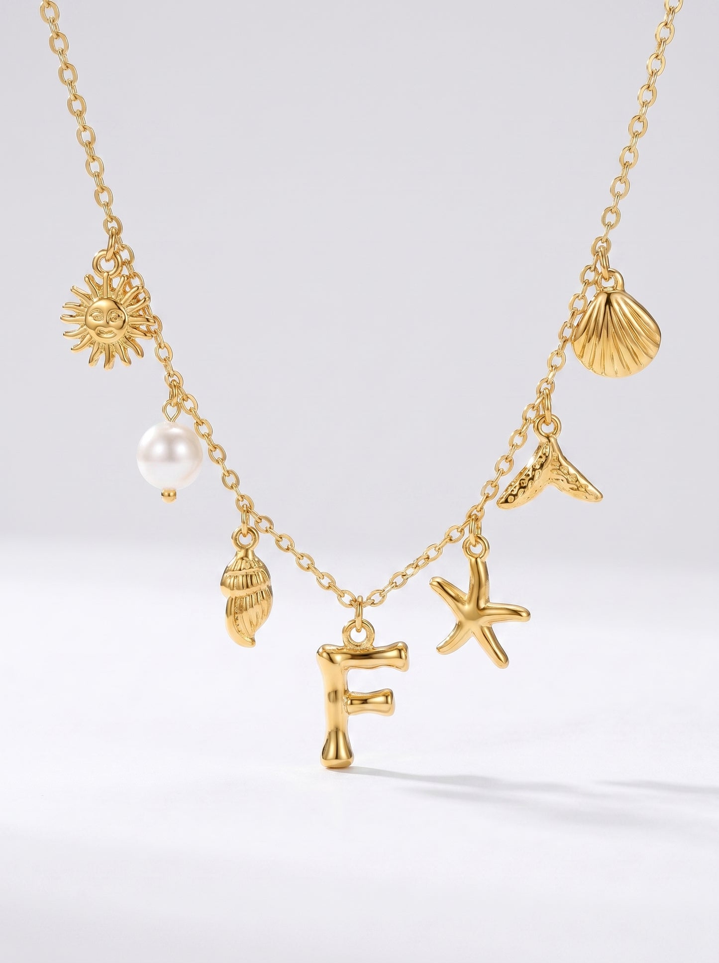 Colar dourado do mar com letra inicial F, estrela-do-mar, conchas, pérola e pendente de sol.