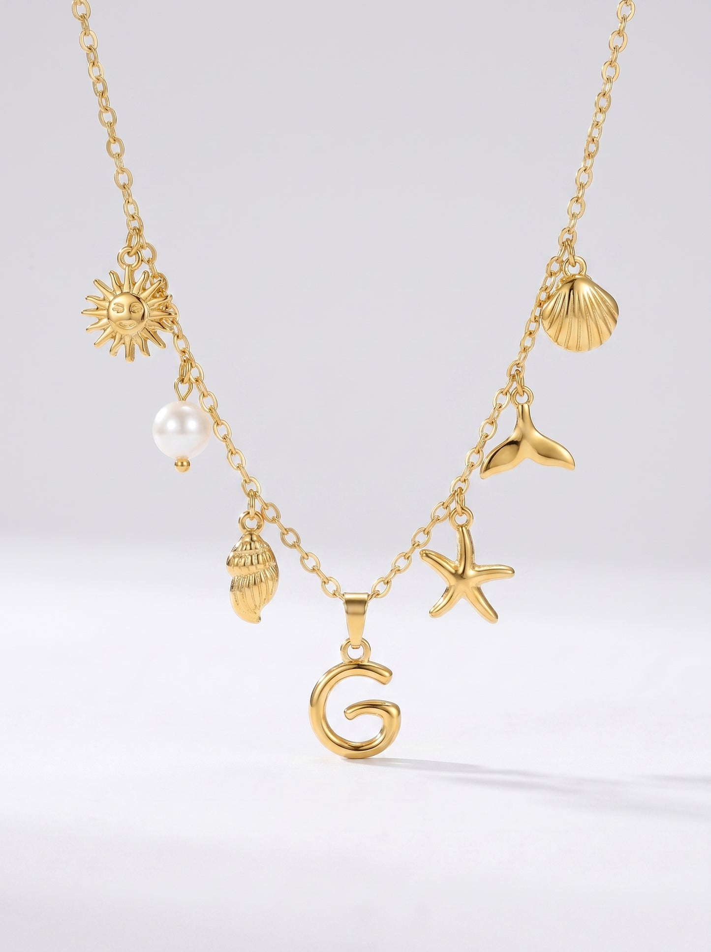Colar dourado do mar com letra inicial G, estrela-do-mar, conchas, pérola e pendente de sol.