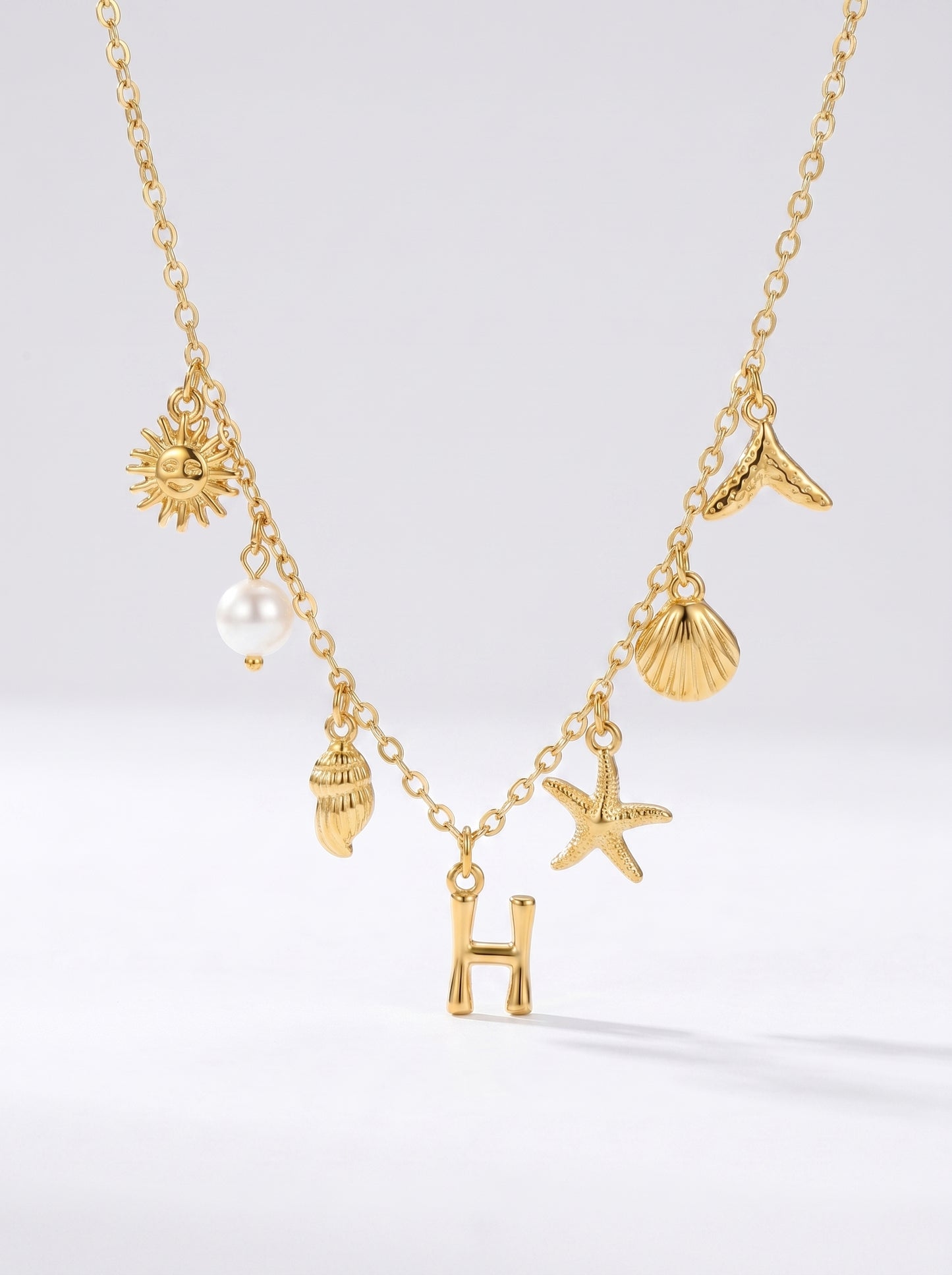 Colar dourado do mar com letra inicial H, estrela-do-mar, conchas, pérola e pendente de sol.