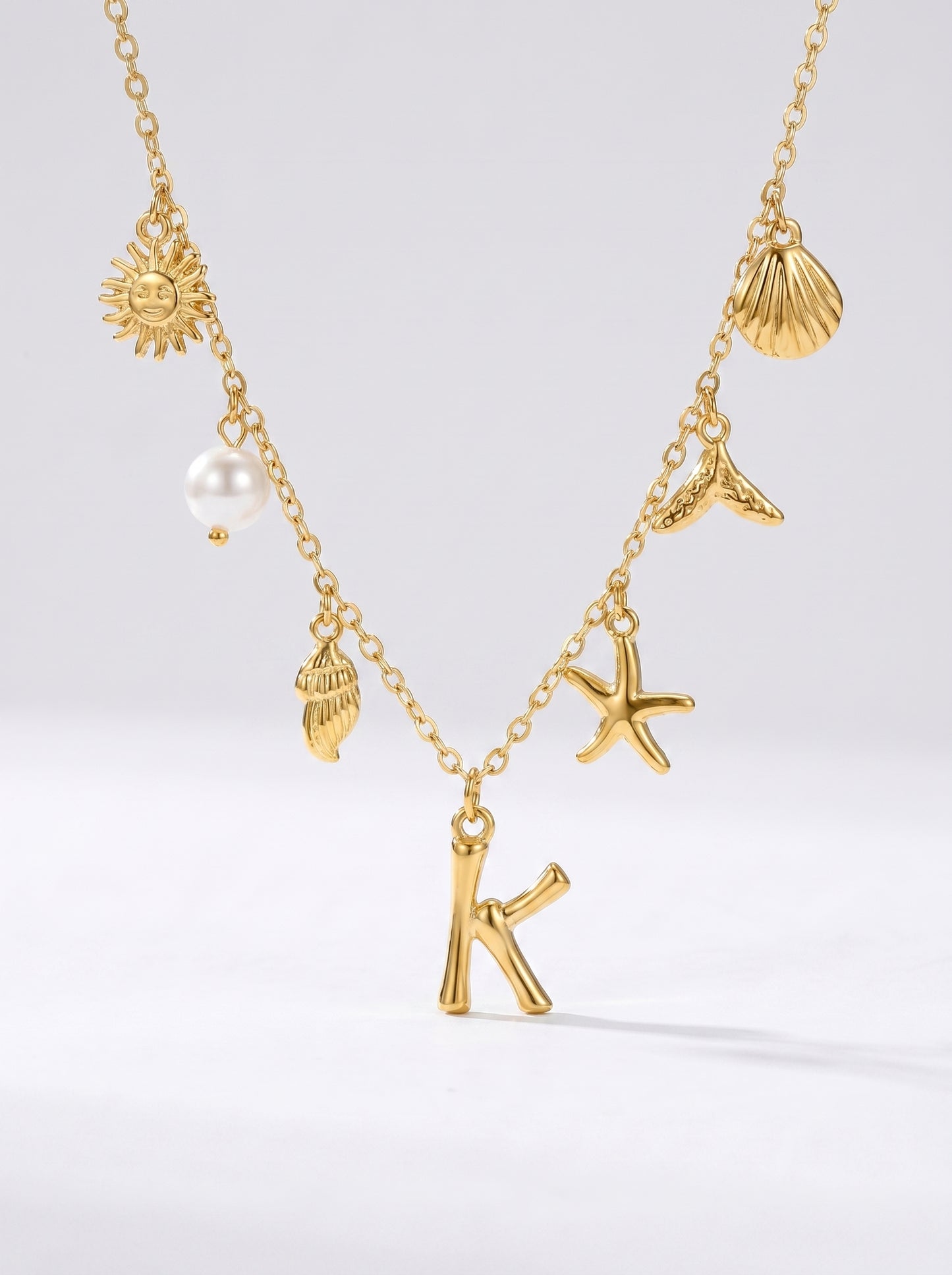 Colar dourado do mar com letra inicial K, estrela-do-mar, conchas, pérola e pendente de sol.