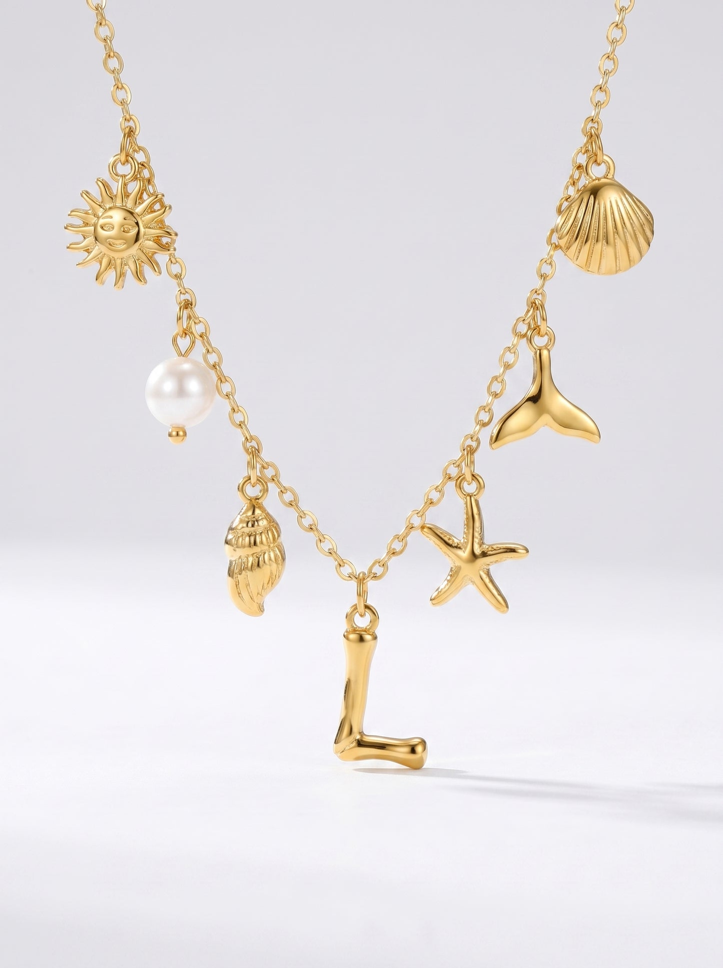 Colar dourado do mar com letra inicial L, estrela-do-mar, conchas, pérola e pendente de sol.