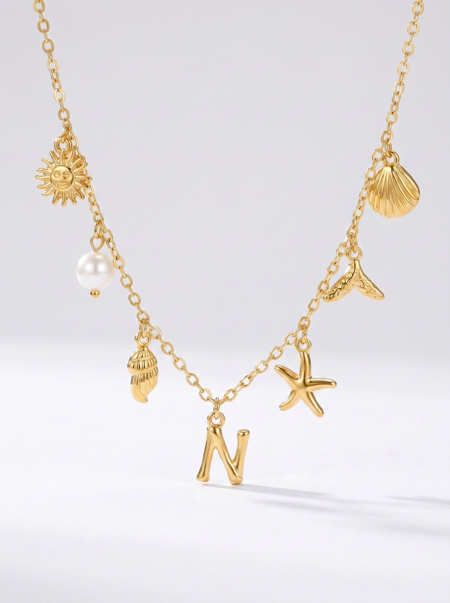 Colar dourado do mar com letra inicial N, estrela-do-mar, conchas, pérola e pendente de sol.