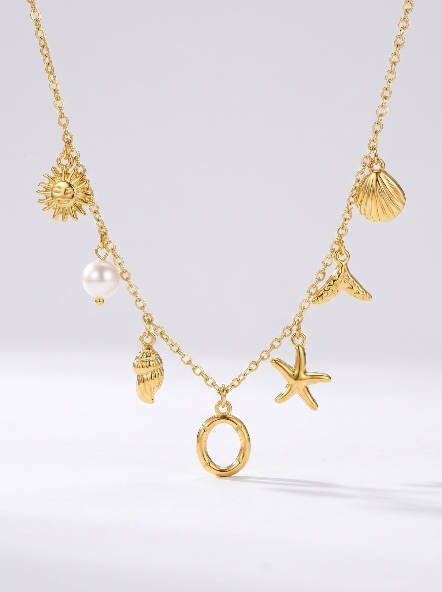 Colar dourado do mar com letra inicial O, estrela-do-mar, conchas, pérola e pendente de sol.