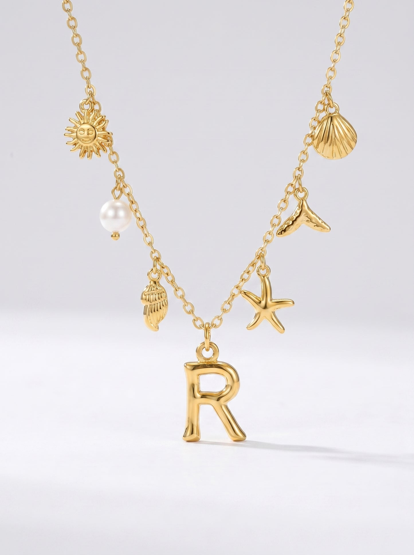 Colar dourado do mar com letra inicial R, estrela-do-mar, conchas, pérola e pendente de sol.