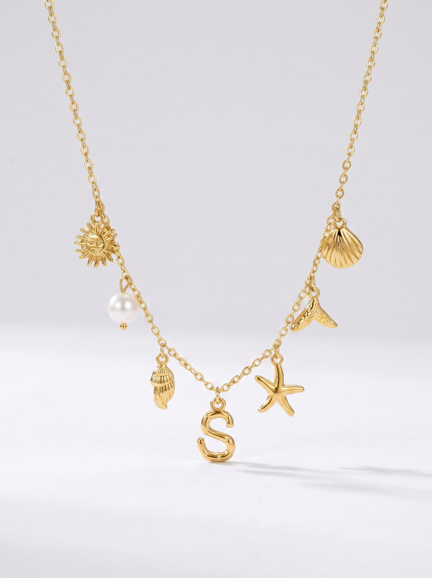 Colar dourado do mar com letra inicial S, estrela-do-mar, conchas, pérola e pendente de sol.