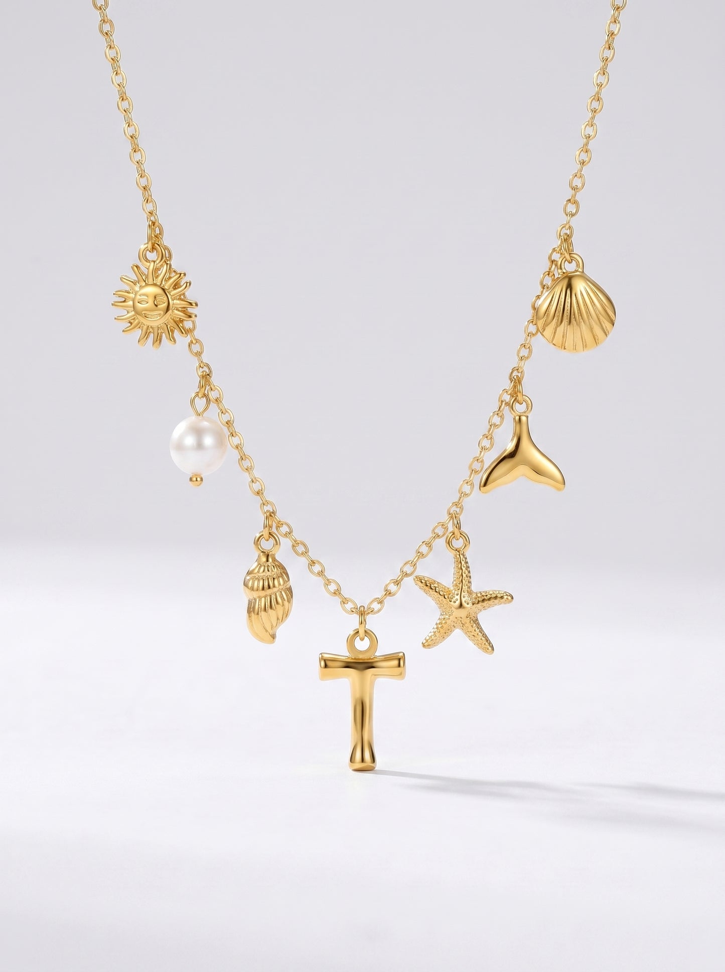 Colar dourado do mar com letra inicial T, estrela-do-mar, conchas, pérola e pendente de sol.