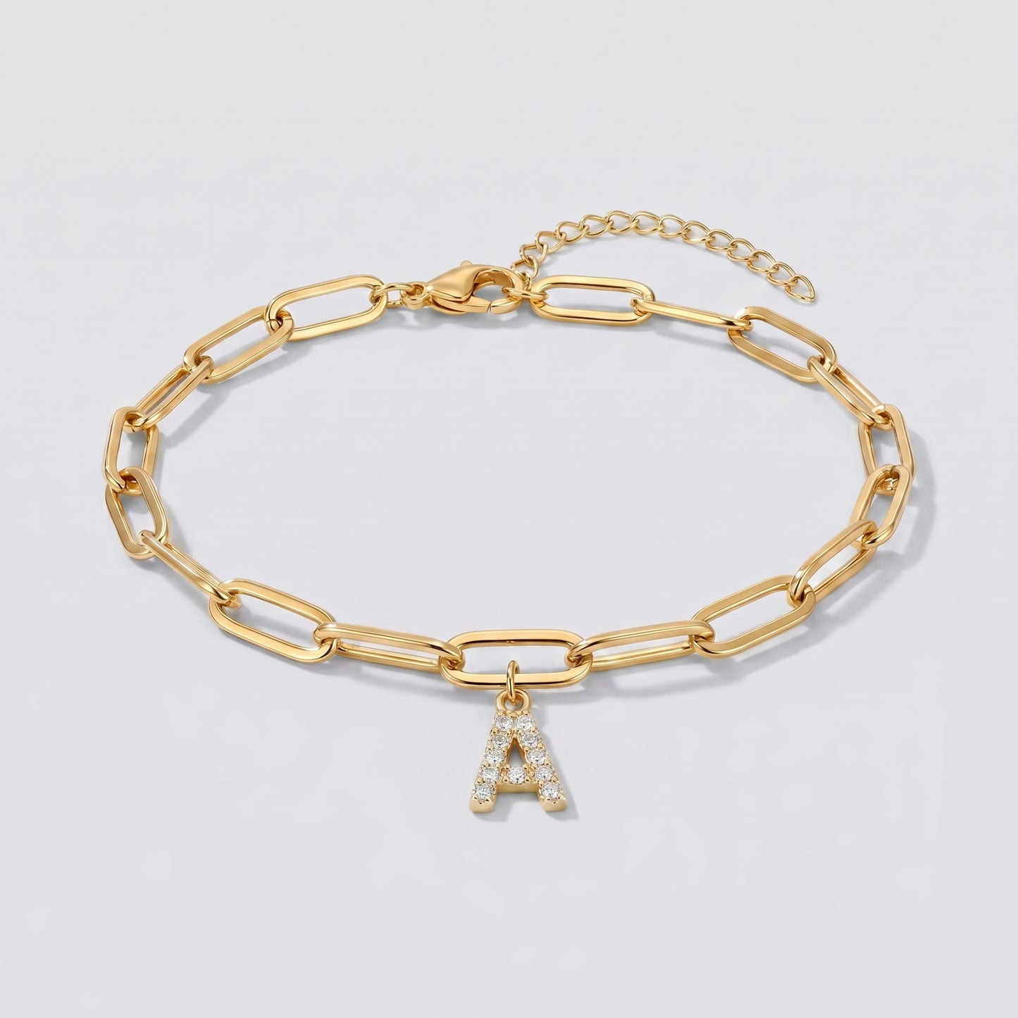 Pulseira dourada com letra inicial A, corrente paperclip e pendente de letra cravejado.
