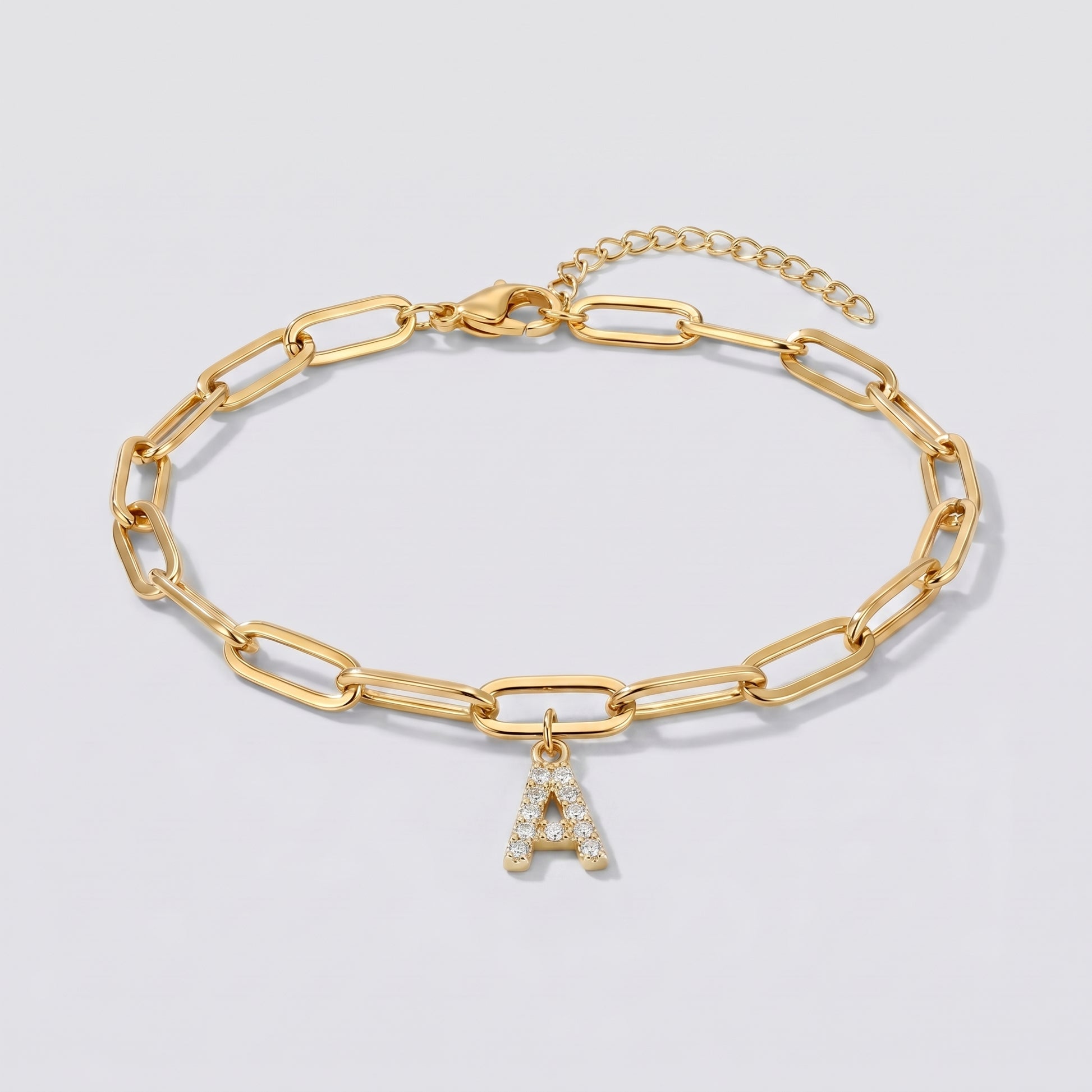 Pulseira dourada com letra inicial A, corrente paperclip e pendente de letra cravejado.
