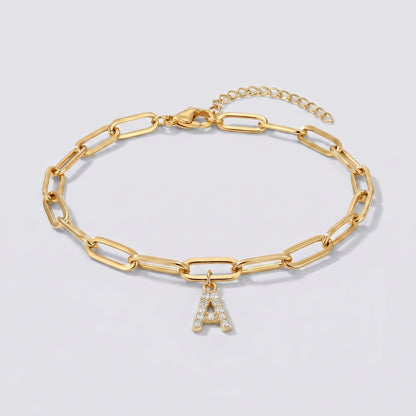 Pulseira dourada com letra inicial A, corrente paperclip e pendente de letra cravejado.
