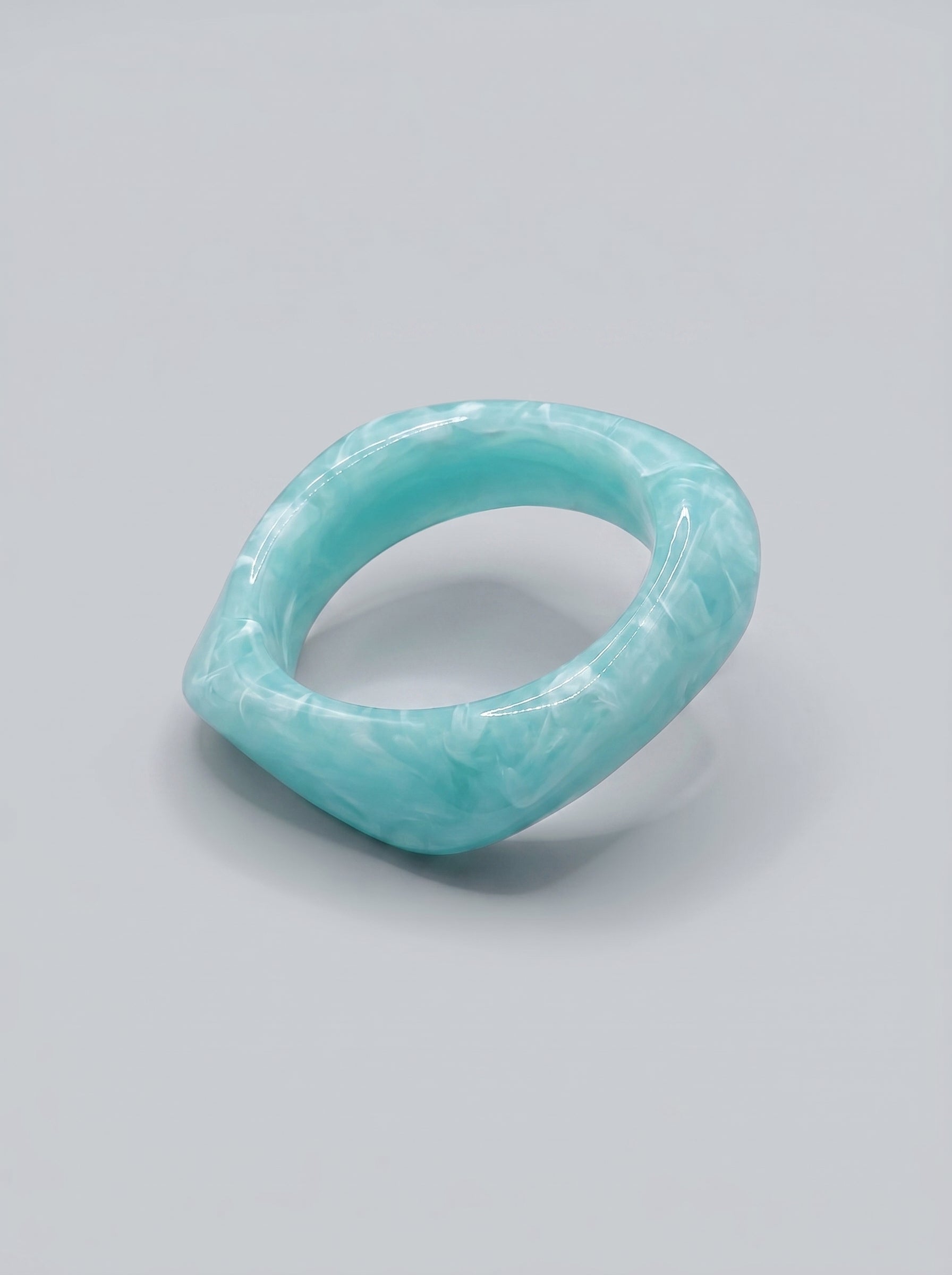 Pulseira Água do Mar em resina marmoreada nos tons azul marinho e turquesa, com design orgânico geométrico e acabamento brilhante, ideal para um look elegante e contemporâneo.
