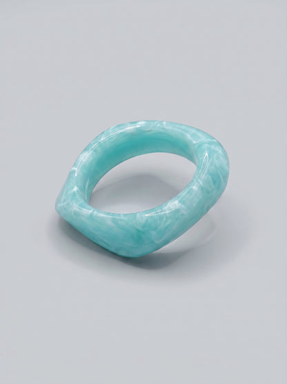 Pulseira Água do Mar em resina marmoreada nos tons azul marinho e turquesa, com design orgânico geométrico e acabamento brilhante, ideal para um look elegante e contemporâneo.
