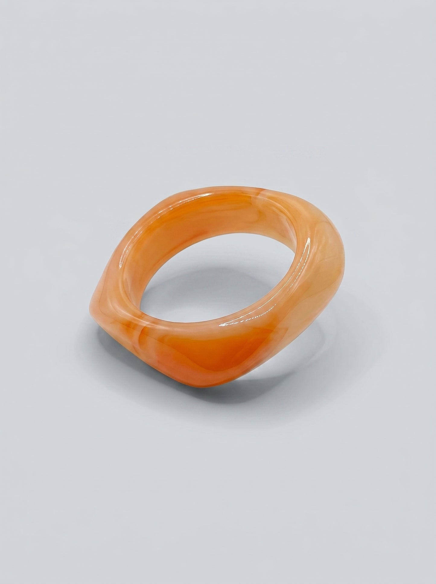 Pulseira Alperce em resina marmoreada nos tons alperce e coral suave, com design orgânico geométrico e acabamento brilhante, ideal para um look elegante e contemporâneo.
