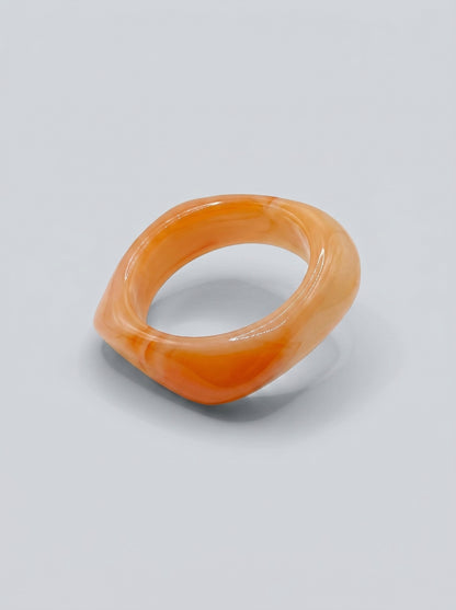 Pulseira Alperce em resina marmoreada nos tons alperce e coral suave, com design orgânico geométrico e acabamento brilhante, ideal para um look elegante e contemporâneo.
