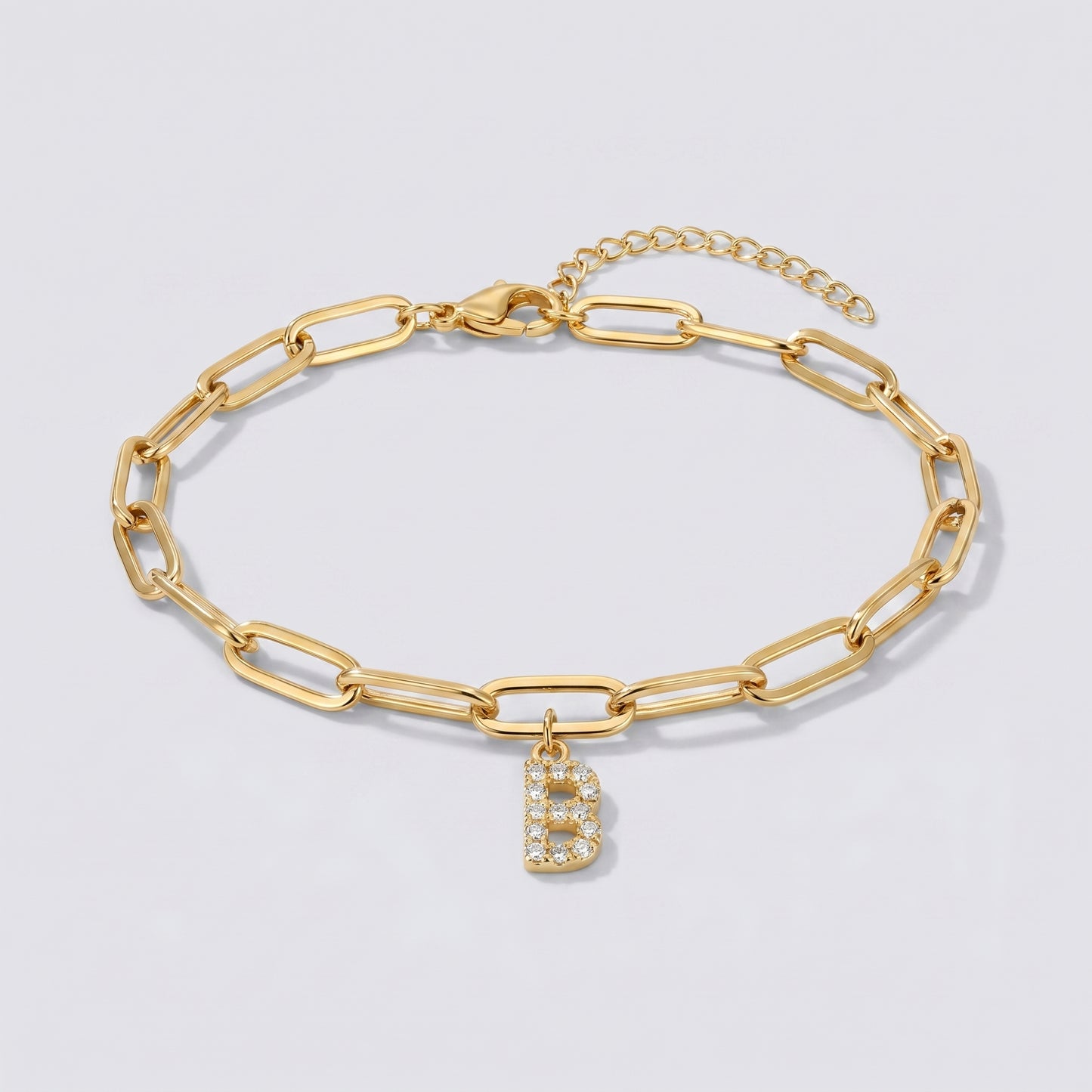 Pulseira dourada com letra inicial B, corrente paperclip e pendente de letra cravejado.