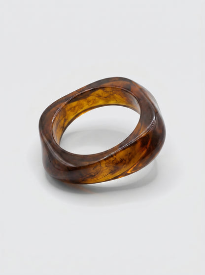 Pulseira Canela em resina marmoreada nos tons canela e âmbar escuro, com design orgânico geométrico e acabamento brilhante, ideal para um look elegante e contemporâneo.

