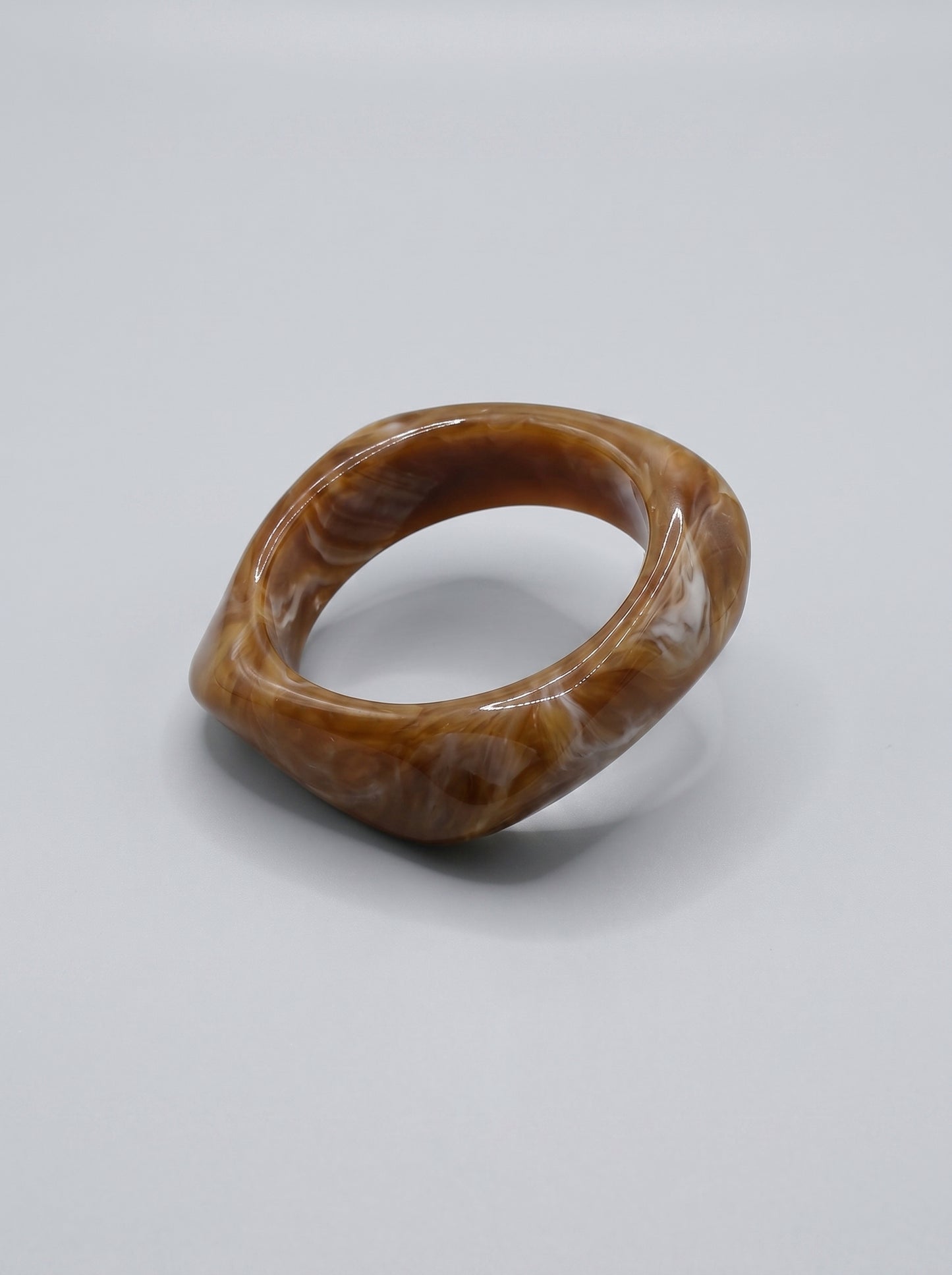 Pulseira Caramelo em resina marmoreada nos tons caramelo e dourado, com design orgânico geométrico e acabamento brilhante, ideal para um look elegante e contemporâneo.
