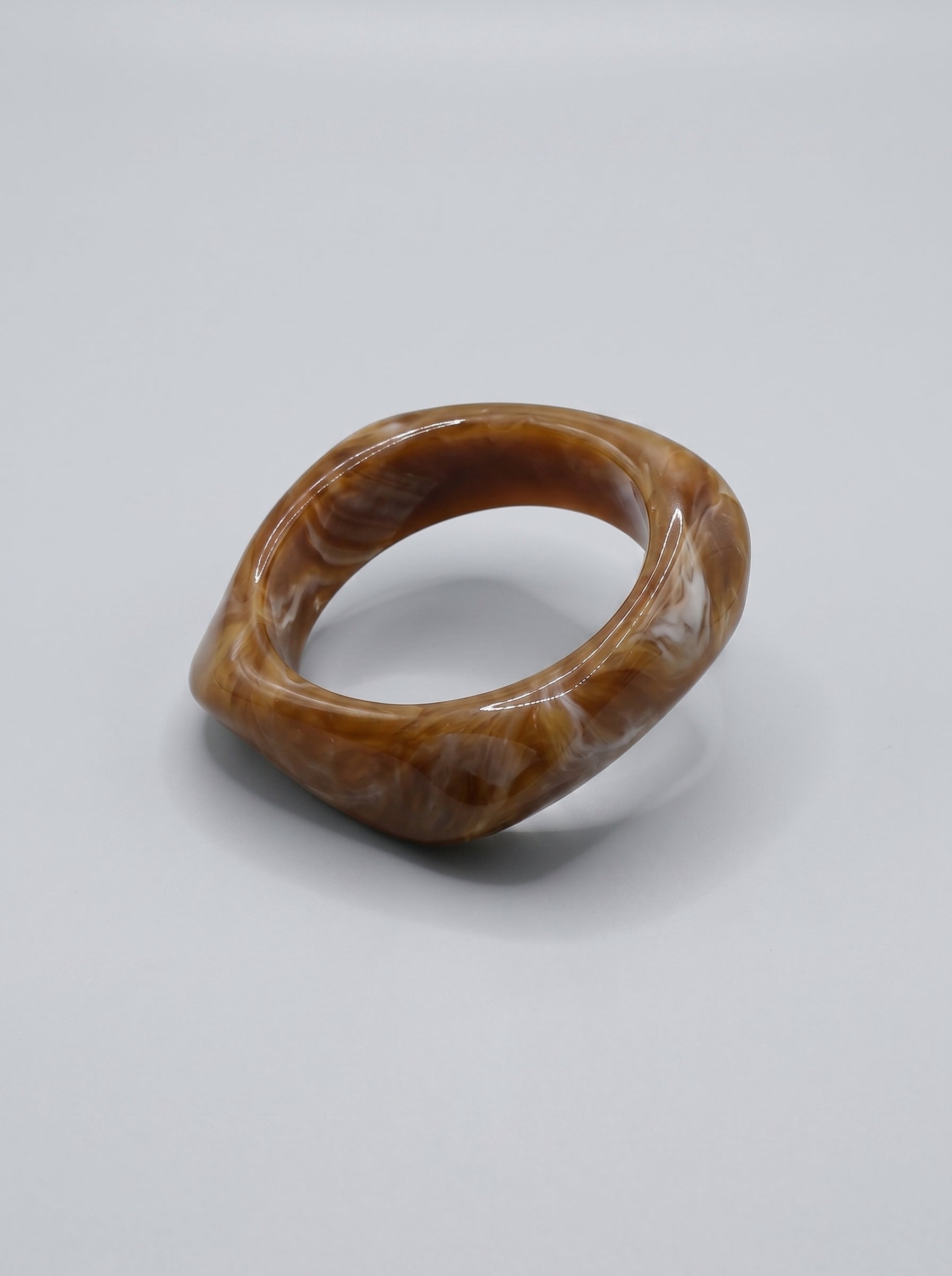 Pulseira Caramelo em resina marmoreada nos tons caramelo e dourado, com design orgânico geométrico e acabamento brilhante, ideal para um look elegante e contemporâneo.
