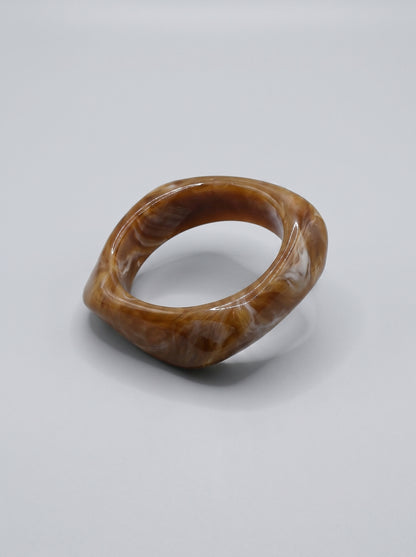 Pulseira Caramelo em resina marmoreada nos tons caramelo e dourado, com design orgânico geométrico e acabamento brilhante, ideal para um look elegante e contemporâneo.
