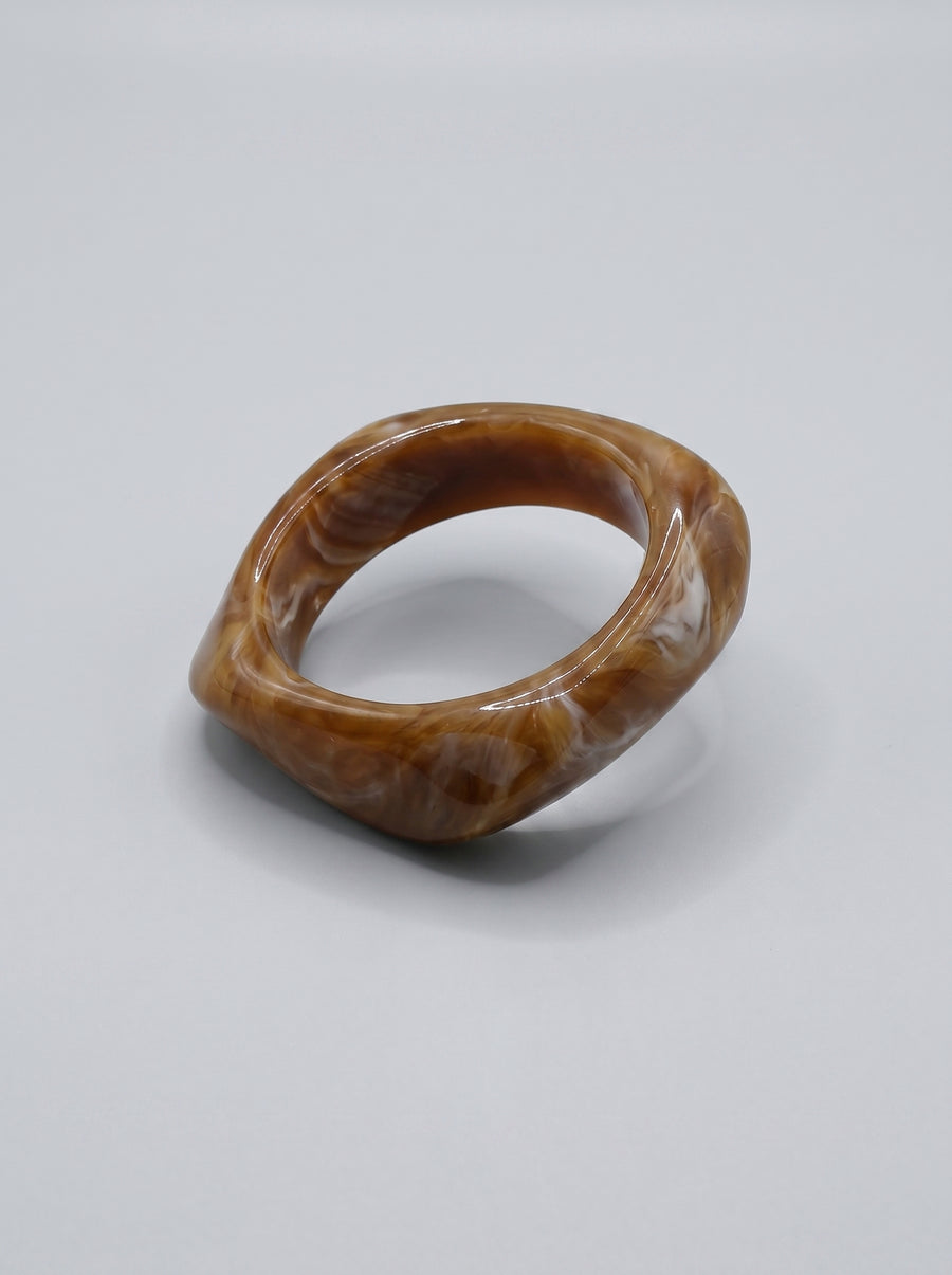 Pulseira Caramelo em resina marmoreada nos tons caramelo e dourado, com design orgânico geométrico e acabamento brilhante, ideal para um look elegante e contemporâneo.
