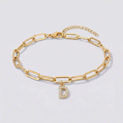 Pulseira dourada com letra inicial D, corrente paperclip e pendente de letra cravejado.
