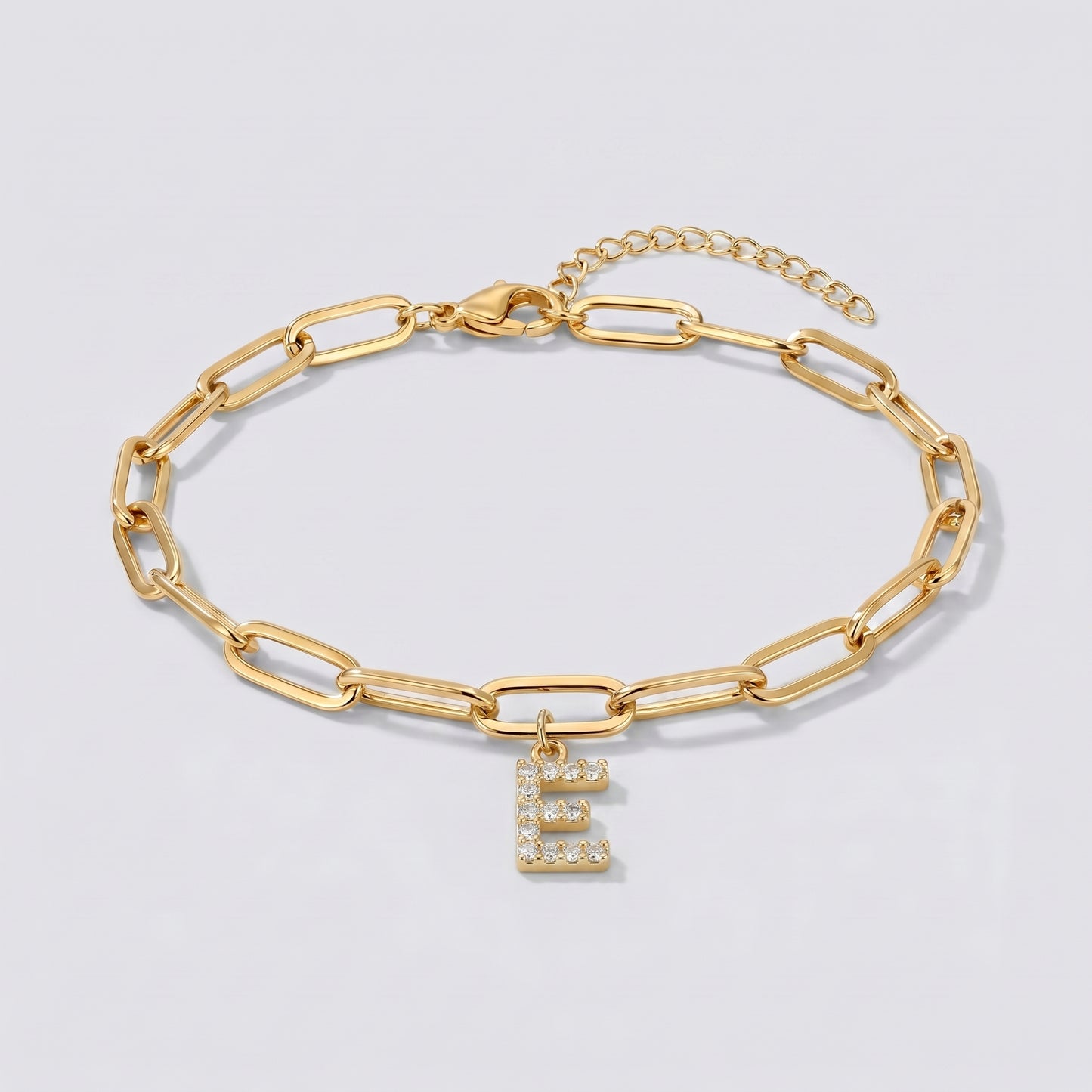 Pulseira dourada com letra inicial E, corrente paperclip e pendente de letra cravejado.