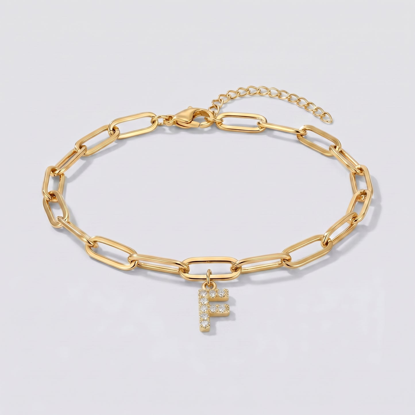Pulseira dourada com letra inicial F, corrente paperclip e pendente de letra cravejado.