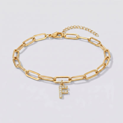Pulseira dourada com letra inicial F, corrente paperclip e pendente de letra cravejado.