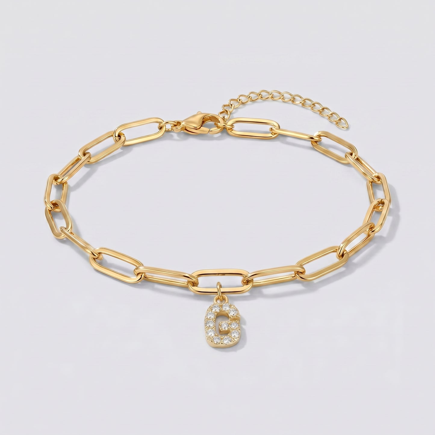Pulseira dourada com letra inicial G, corrente paperclip e pendente de letra cravejado.