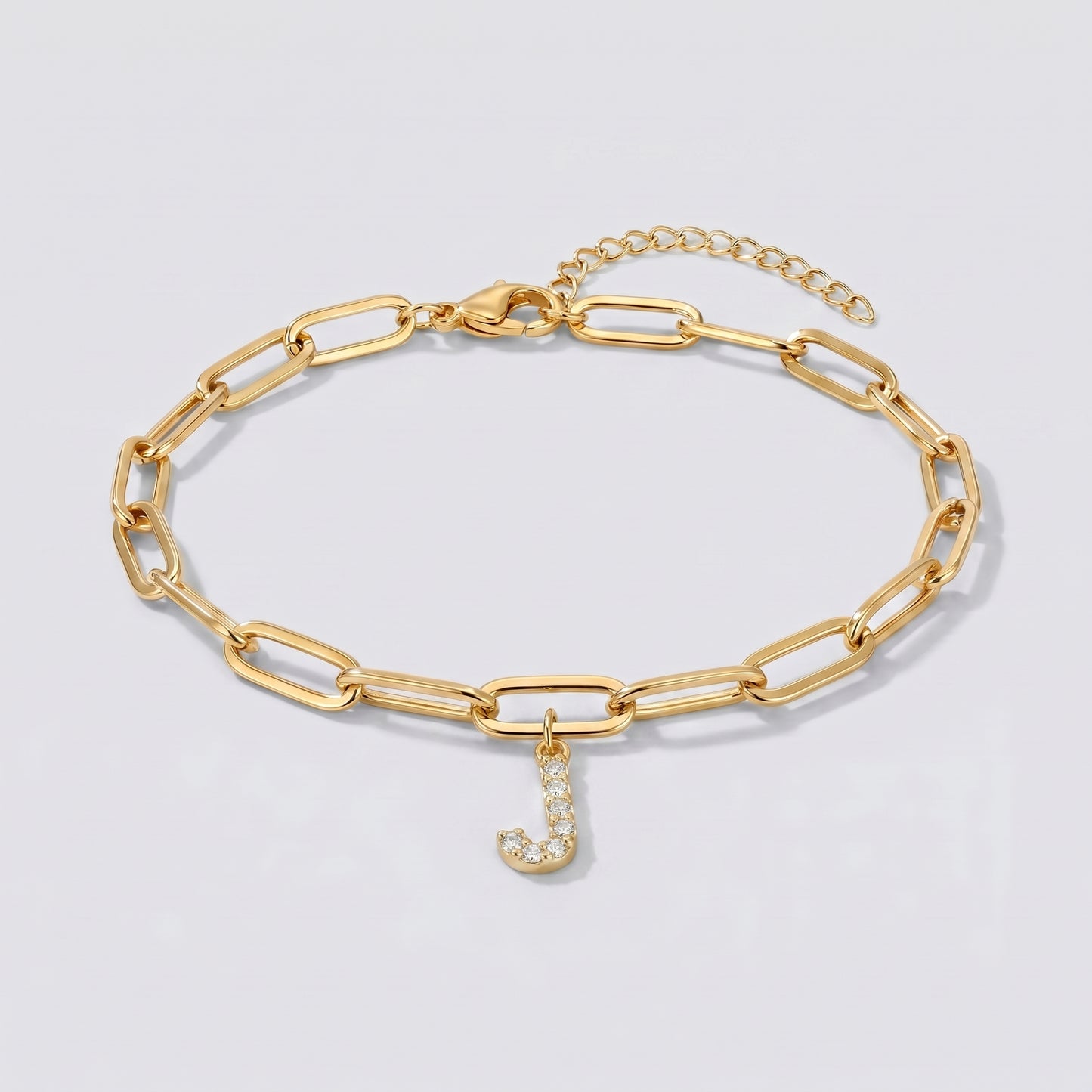 Pulseira dourada com letra inicial J, corrente paperclip e pendente de letra cravejado.