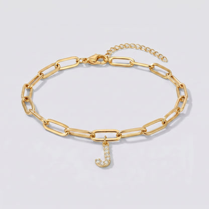 Pulseira dourada com letra inicial J, corrente paperclip e pendente de letra cravejado.