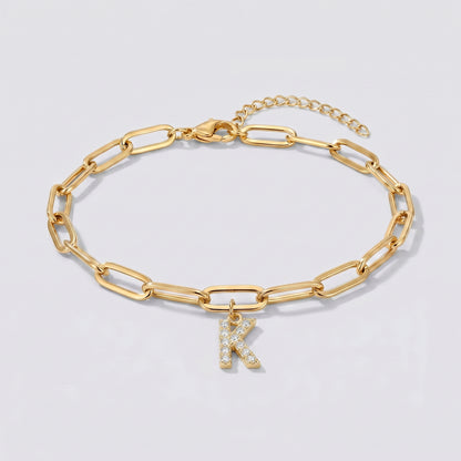 Pulseira dourada com letra inicial K, corrente paperclip e pendente de letra cravejado.