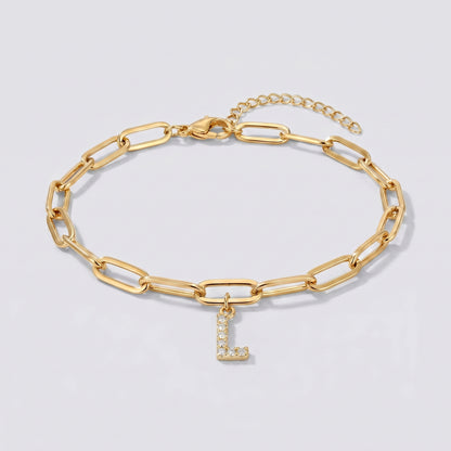 Pulseira dourada com letra inicial L, corrente paperclip e pendente de letra cravejado.