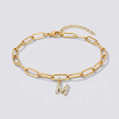 Pulseira dourada com letra inicial M, corrente paperclip e pendente de letra cravejado.