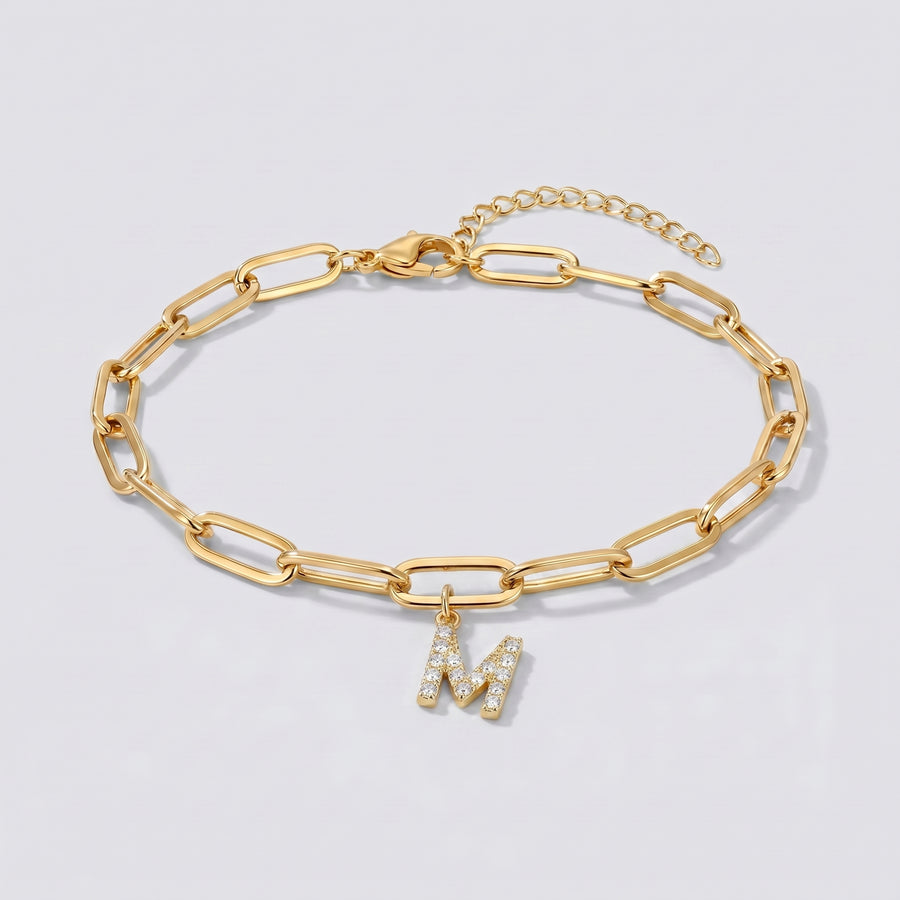 Pulseira dourada com letra inicial M, corrente paperclip e pendente de letra cravejado.