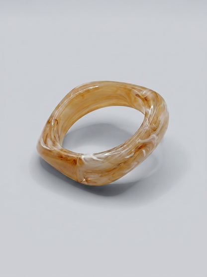 Pulseira Mel Silvestre em resina marmoreada nos tons mel e âmbar, com design geométrico orgânico e acabamento brilhante, ideal para um estilo elegante e contemporâneo.