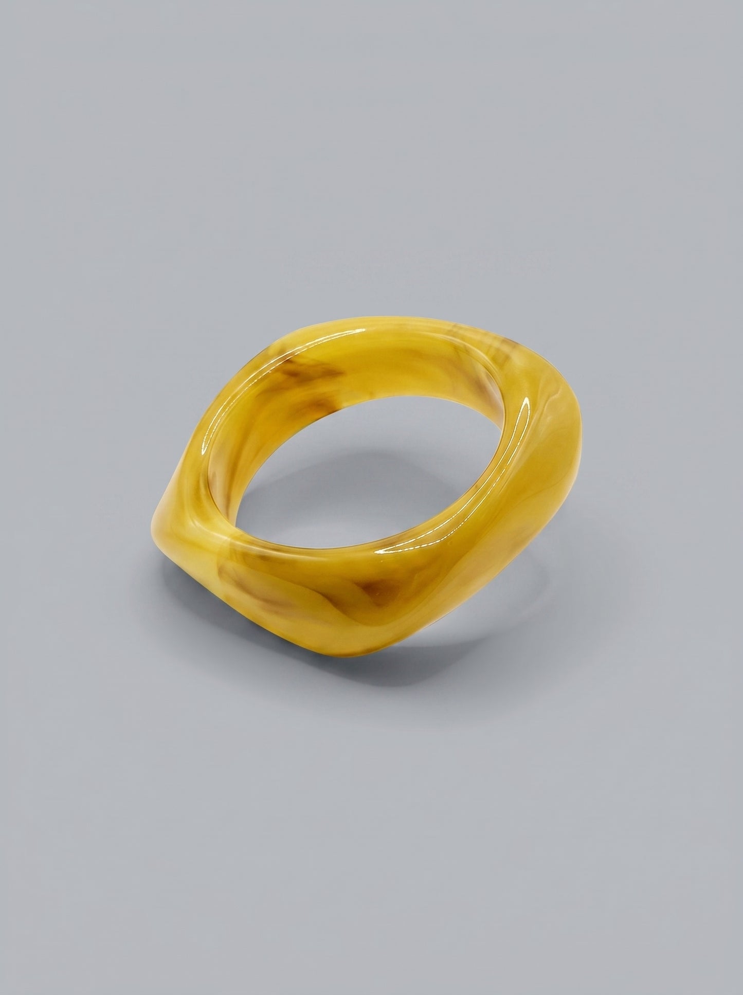 Pulseira Mostarda em resina marmoreada nos tons mostarda e amarelo dourado, com design orgânico geométrico e acabamento brilhante, ideal para um look elegante e contemporâneo.

