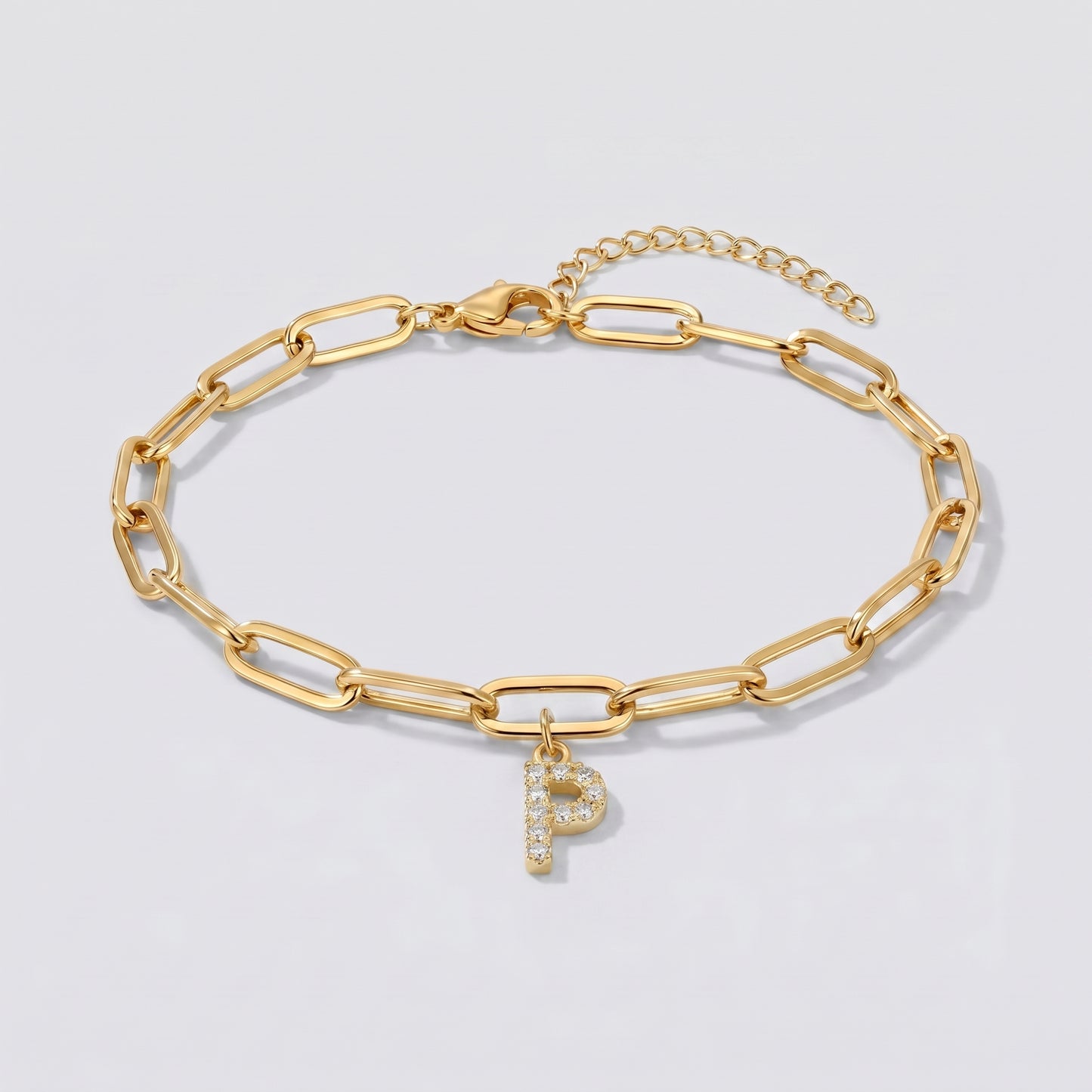 Pulseira dourada com letra inicial P, corrente paperclip e pendente de letra cravejado.