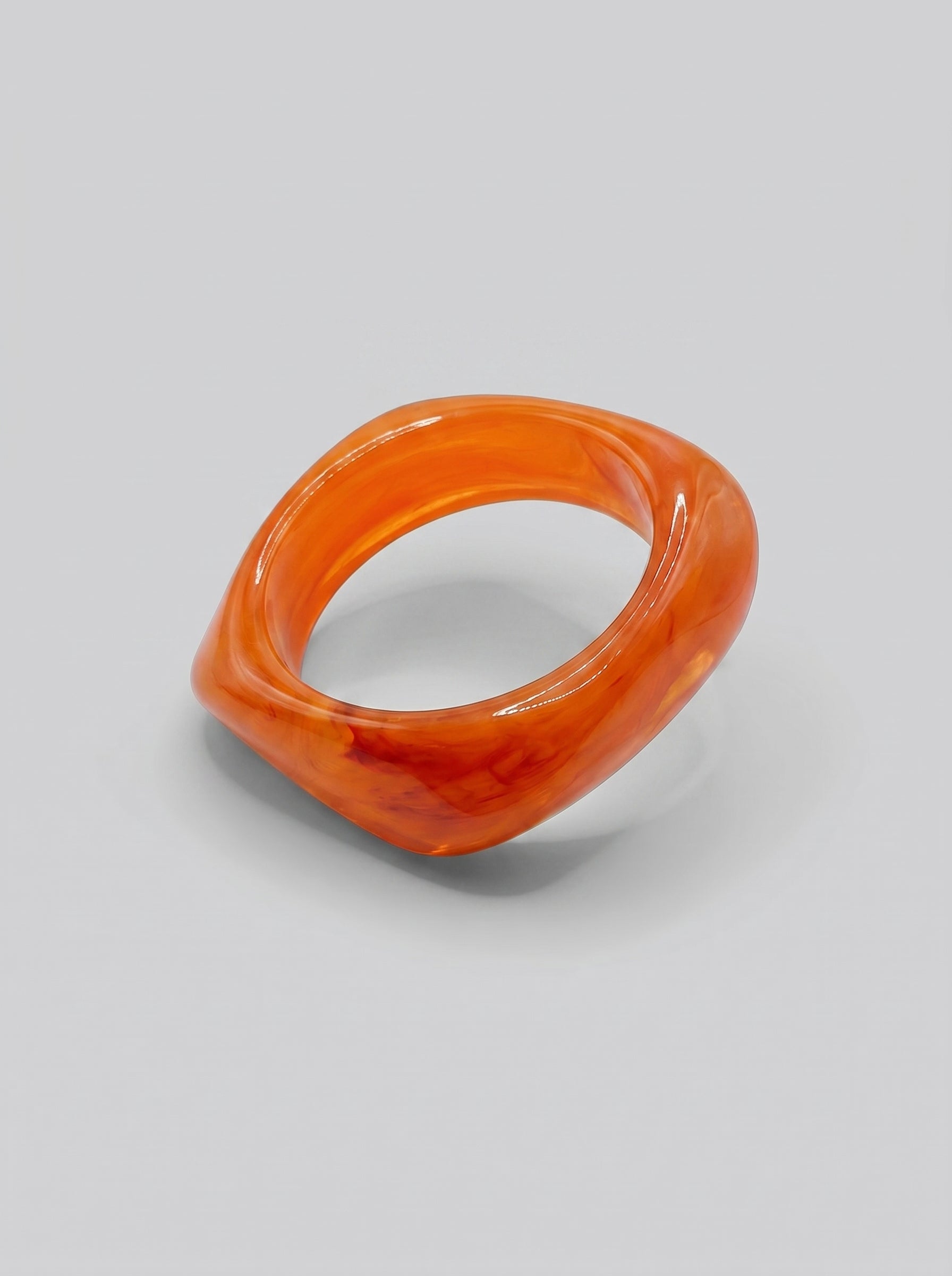Pulseira Pôr do Sol em resina marmoreada nos tons pôr do sol, coral e laranja, com design orgânico geométrico e acabamento brilhante, ideal para um look elegante e contemporâneo.
