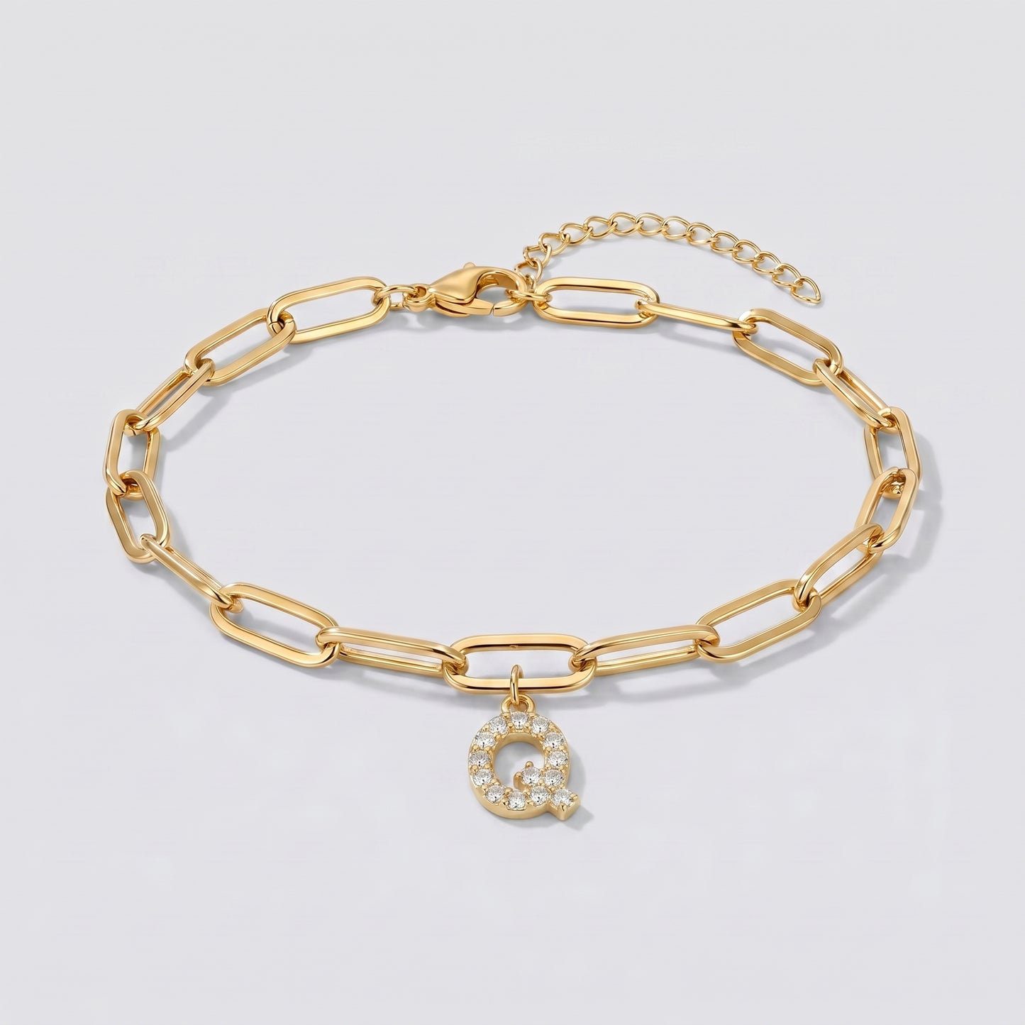 Pulseira dourada com letra inicial Q, corrente paperclip e pendente de letra cravejado.