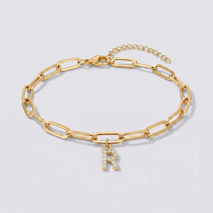 Pulseira dourada com letra inicial R, corrente paperclip e pendente de letra cravejado.