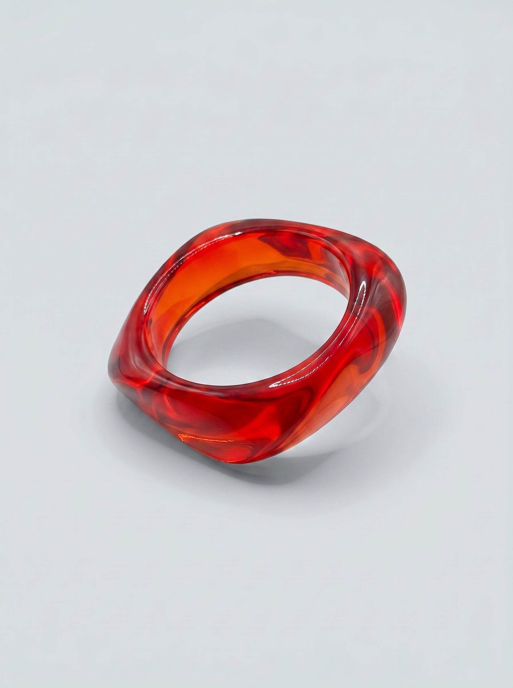 Pulseira Ruby em resina marmoreada nos tons ruby e vermelho intenso, com design orgânico geométrico e acabamento brilhante, ideal para um look elegante e contemporâneo.
