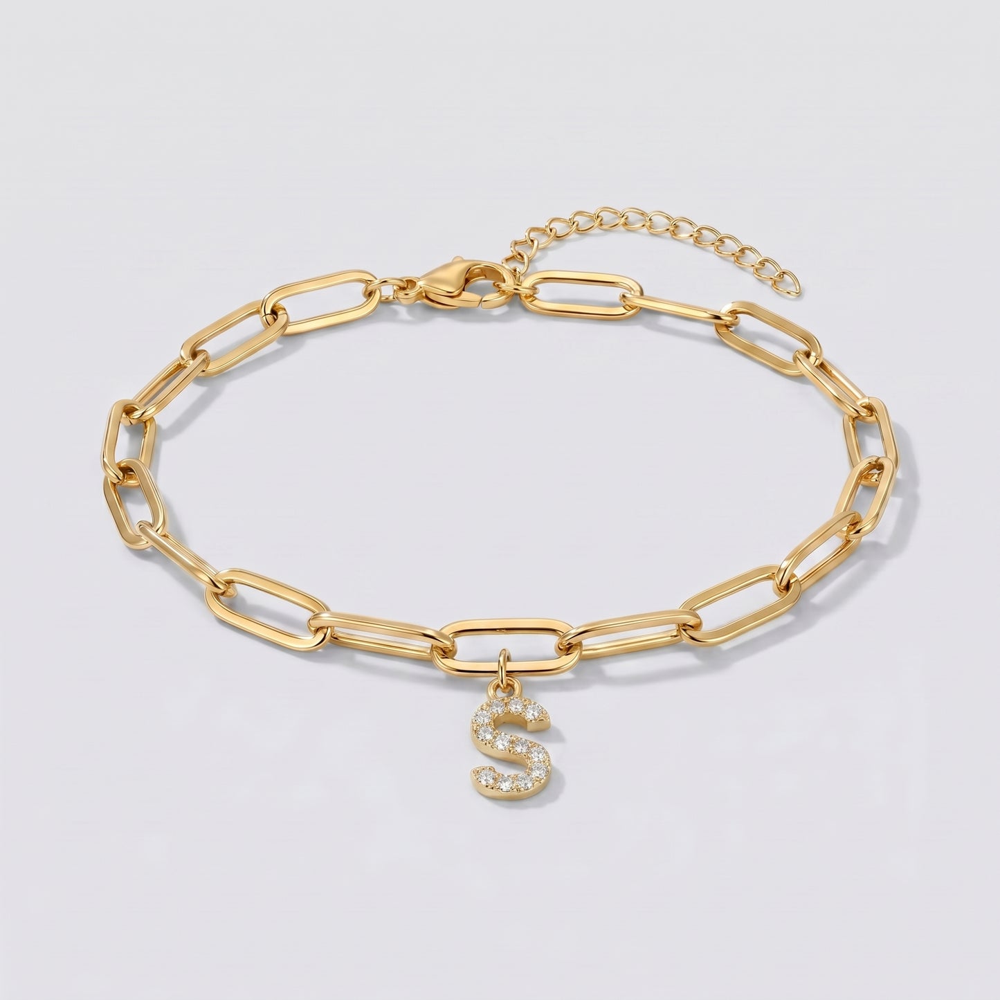 Pulseira dourada com letra inicial S, corrente paperclip e pendente de letra cravejado.