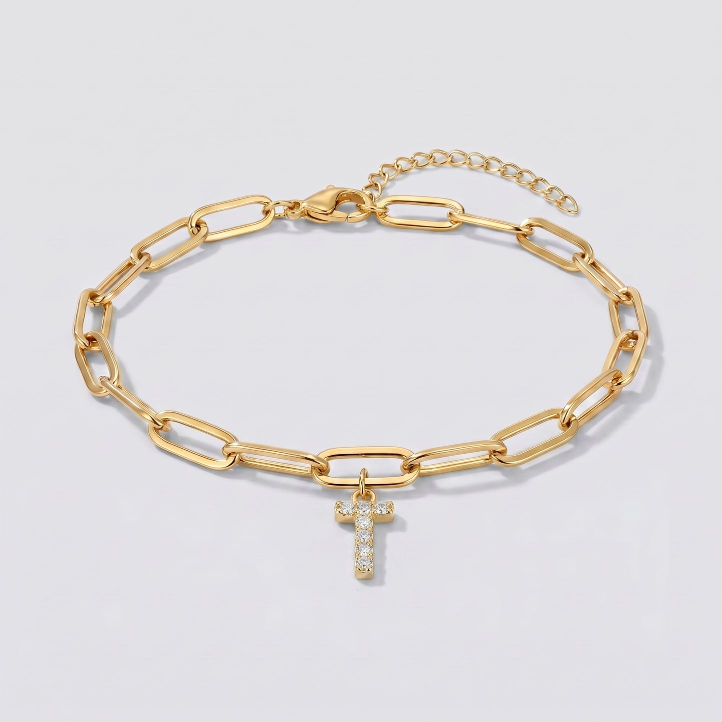 Pulseira dourada com letra inicial T, corrente paperclip e pendente de letra cravejado.