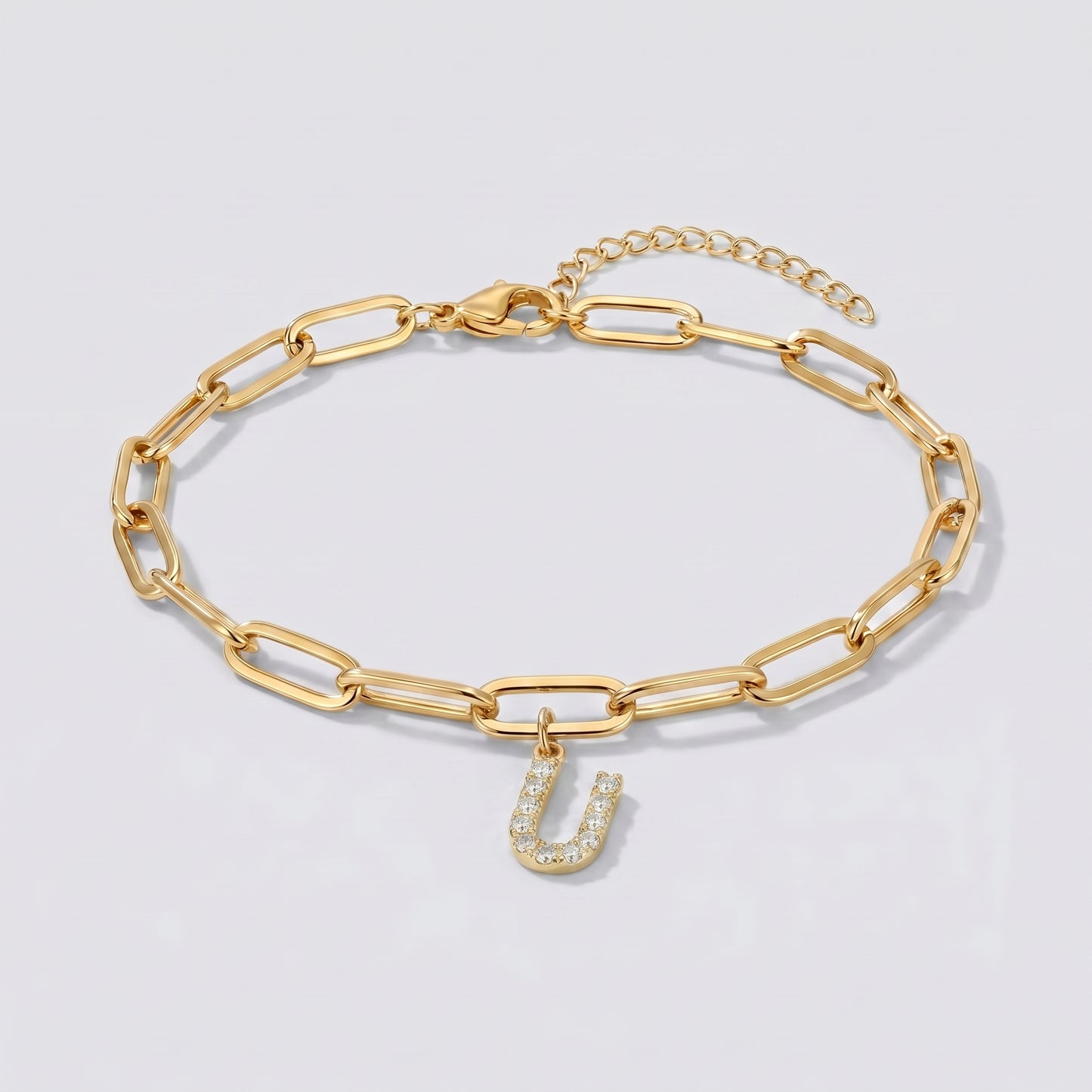 Pulseira dourada com letra inicial U, corrente paperclip e pendente de letra cravejado.