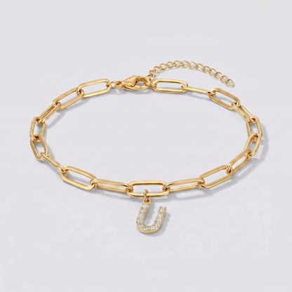 Pulseira dourada com letra inicial U, corrente paperclip e pendente de letra cravejado.